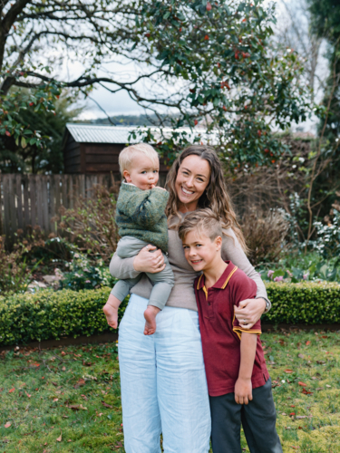 Aussie mum stands in the garden carrying toddler while hugging the older son - Australian Stock Image