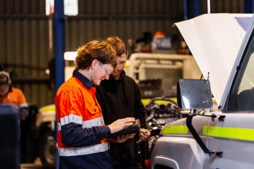 Aussie workman using digital diagnostics tool working on car vehicle engine in mechanics workshop - Australian Stock Image