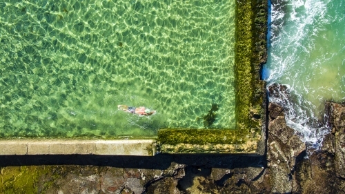 A mature man swimming laps in the Austinmer Rock Pool as waves lap the edges