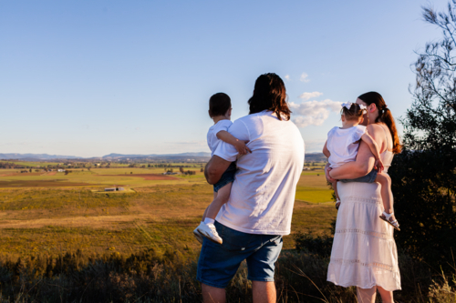Australian family with mum and dad holding children looking out over farmland  view - Australian Stock Image