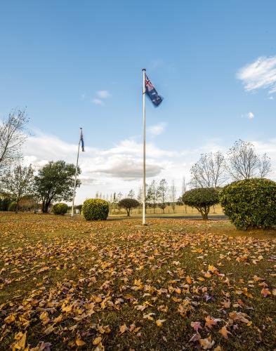 Australian flag moving in breeze with autumn eaves under flag pole - Australian Stock Image