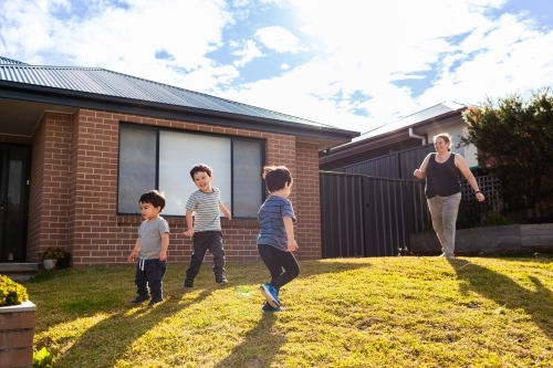 Australian mum running around with young boys in front yard of suburban home - Australian Stock Image