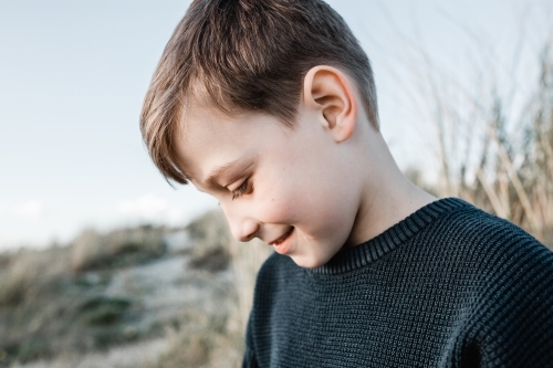 Autistic boy sitting in sand dunes looking down - Australian Stock Image