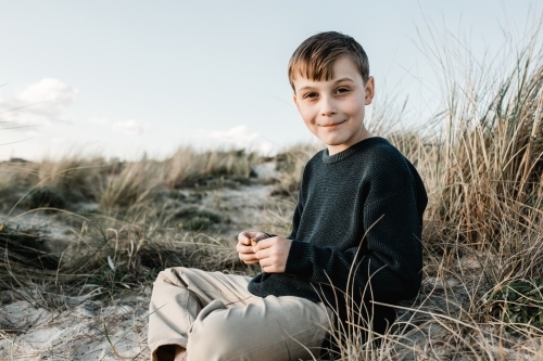 Autistic Boy sitting on a sand dune in the grass - Australian Stock Image