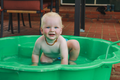Baby boy playing in green plastic shell pool in summer - Australian Stock Image