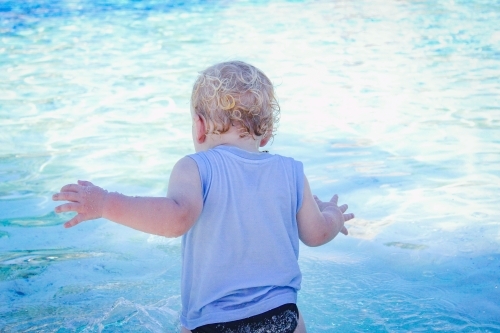 Baby boy standing at the edge of a sparkling blue resort swimming pool - Australian Stock Image