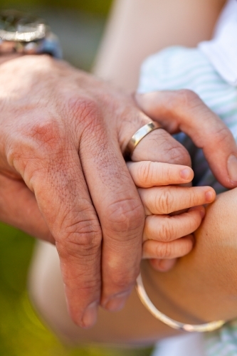 Baby hand wrapped around parents finger wearing wedding band ring - family concept - Australian Stock Image