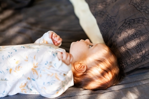 Baby lying on bed looking up with morning sunlight coming through window