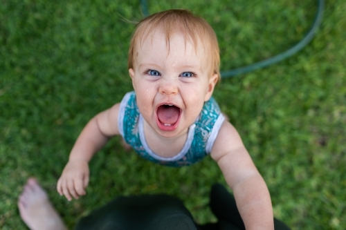 Baby with huge smile looking up at mum while pulling up to stand - Australian Stock Image