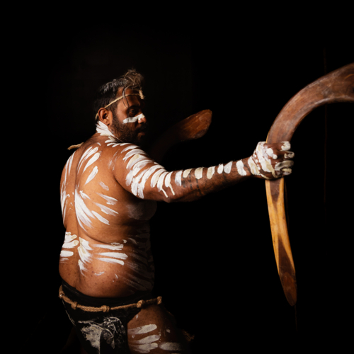 Back of Aboriginal male holding up boomerang to the side - Australian Stock Image