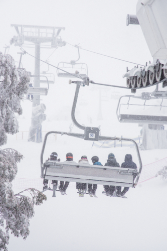 Back of chairlift with 6 skiers going up mountain in the snow - Australian Stock Image