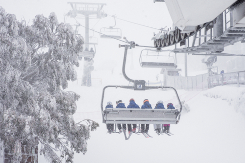 Back of chairlift with 6 skiers going up mountain in the snow - Australian Stock Image