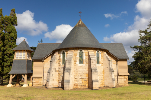 Back of historic stone chapel on green lawn with blue sky - Australian Stock Image