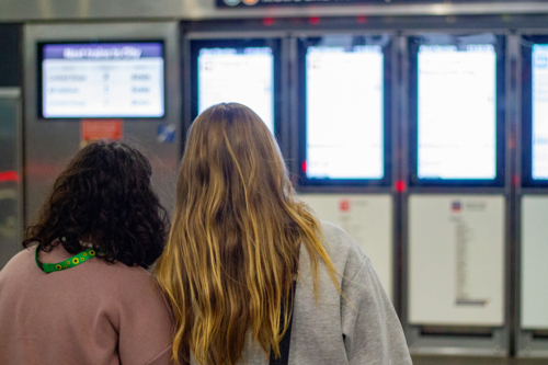Back profile of two young women standing facing a row of digital information screens - Australian Stock Image