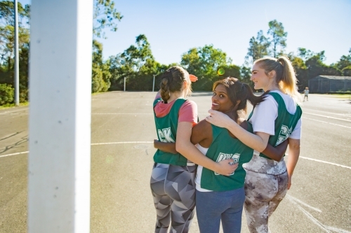 back shot of three young female athletes smiling in a field on a sunny day with trees and clear sky - Australian Stock Image