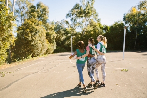 back shot of three young female athletes walking in a field on a sunny day with trees and clear sky - Australian Stock Image