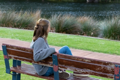 Back view of young woman sitting on park bench - Australian Stock Image