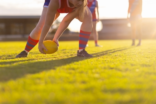 backlit scene with football player picking up football from ground - Australian Stock Image