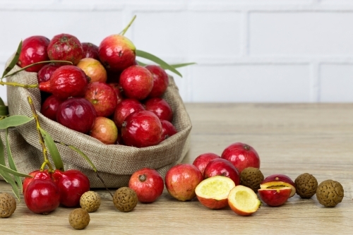 Bag of quandongs on wooden bench, white brick background - Australian Stock Image
