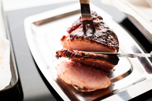 baked ham getting carved on a carving tray - Australian Stock Image