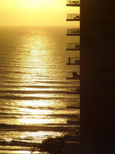 Balconies of a high rise building silhouetted against sunrise across water