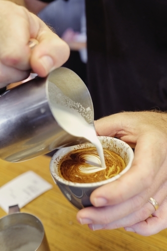 Barista pouring milk to make coffee art - Australian Stock Image