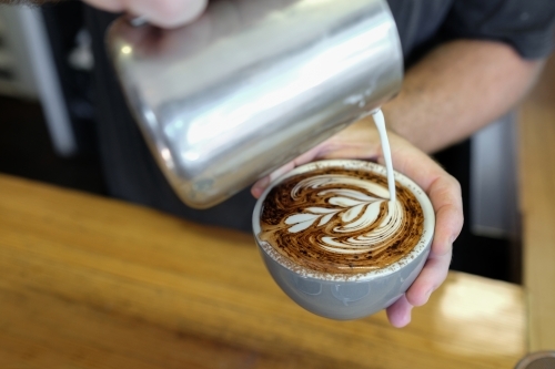 Barista pouring milk to make coffee cappuccino art - Australian Stock Image