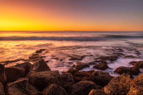 Barnacle covered rocks at sunset with waves crashing - Australian Stock Image