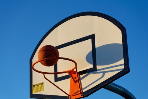 Basketball hoop and ball against a blue sky at sunset at a park - Australian Stock Image