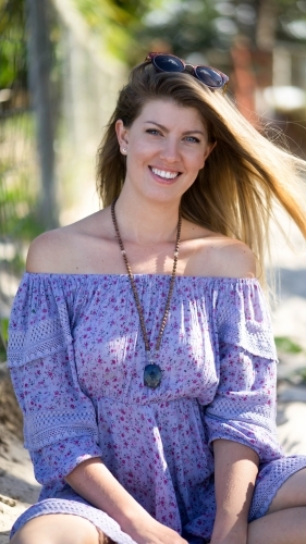 Beach girl in off-shoulder purple dress sitting on sand - Australian Stock Image