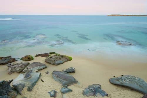 Beach, rocks and ocean at sunset with blurred motion of waves - Australian Stock Image