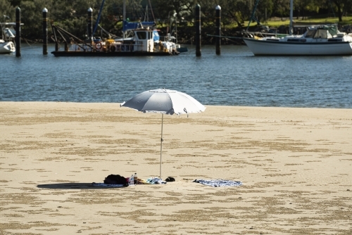 Beach umbrella in beach each scene at rivers edge with boats moored in water