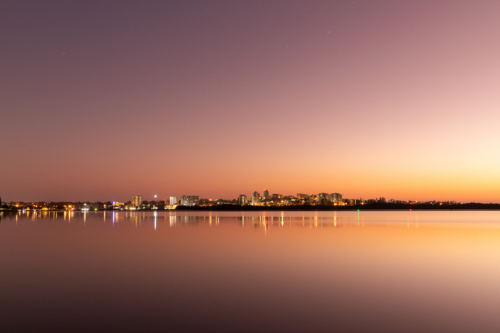 Beachside town in the distance lit up before dawn across inlet - Australian Stock Image