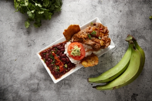 Beans rice and meat dish served in a rectangular plate on a concrete counter with green banana. - Australian Stock Image