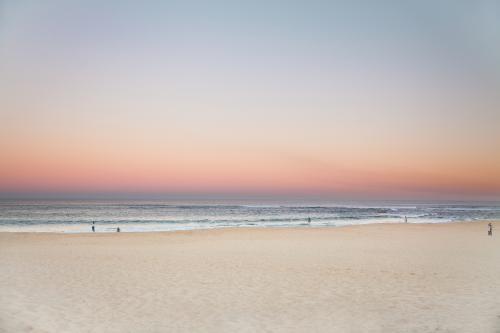Beautiful sunset over a sandy beach with people in the distance - Australian Stock Image