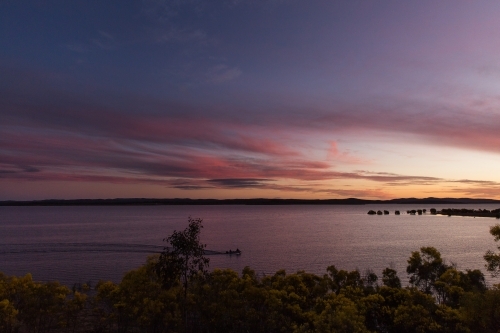 Beautiful sunset over large dam of water with wattle trees in foreground - Australian Stock Image
