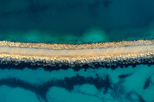 Bird's eye view of a path along a rocky groyne cutting through the ocean waters - Australian Stock Image