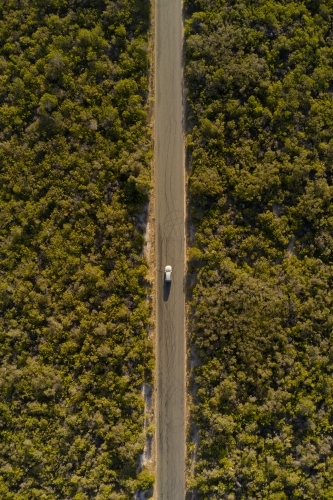 Bird's eye view of a small SUV driving on a coastal road towards a beach