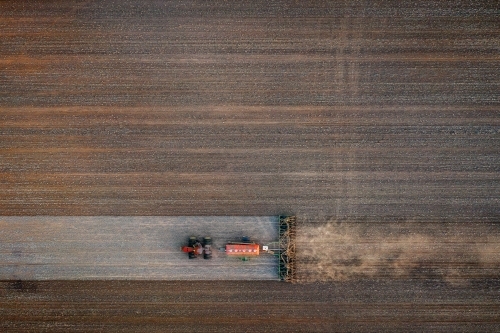 Birds eye view of tractor seeding a dusty paddock
