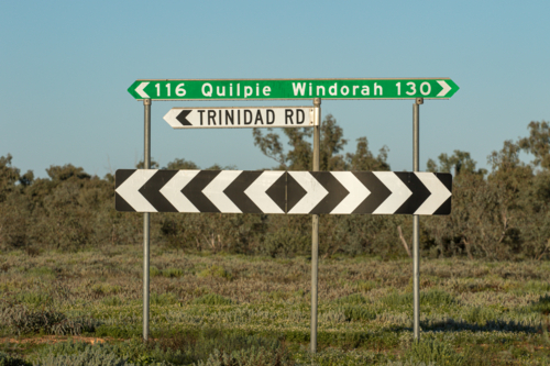 Black and white chevron road sign underneath direction and distance signs - Australian Stock Image