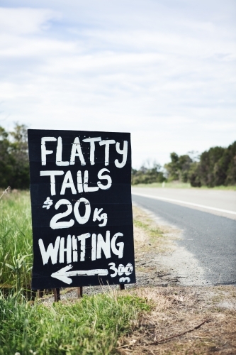 Black and white roadside sign advertising flathead tails vertical