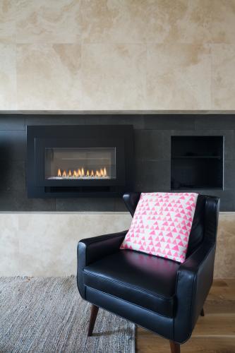 Black leather armchair and pink cushion next to warm cosy fireplace - Australian Stock Image