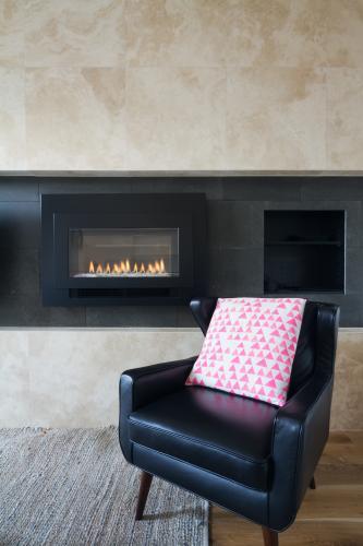 Black leather armchair and pink cushion next to warm cosy fireplace