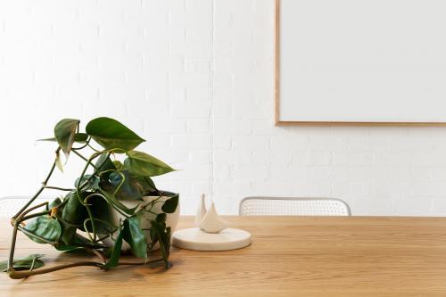 Blank framed artwork on white wall with scandi styled interior objects on wooden table