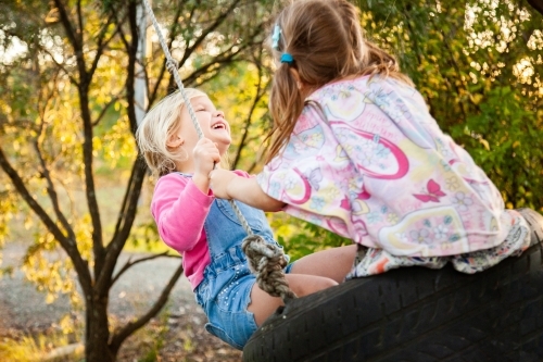 Blond and brunette little girls laughing on swing together