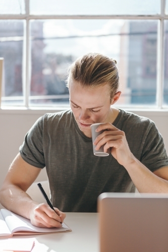 Blond creative man drinking coffee while working
