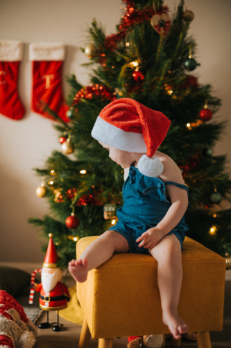 blonde girl sits on a yellow stool by a Christmas tree - Australian Stock Image