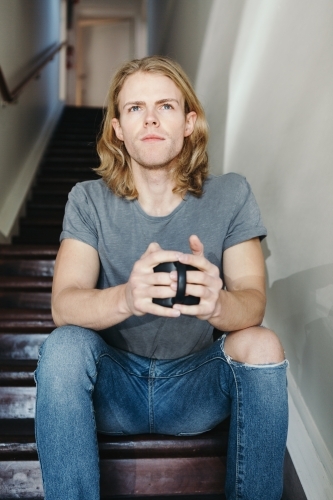 Blonde guy sitting on stairs with a mug of coffee - Australian Stock Image