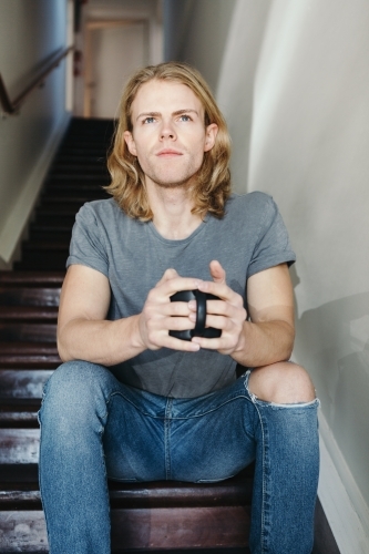 Blonde guy sitting on stairs with a mug of coffee