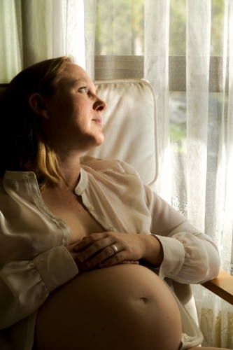Blonde lady in mid-thirties sitting and caressing her pregnant belly.